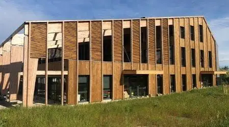 Bâtiment de deux étages entièrement habillé de bardage bois, avec des brise-soleil verticaux