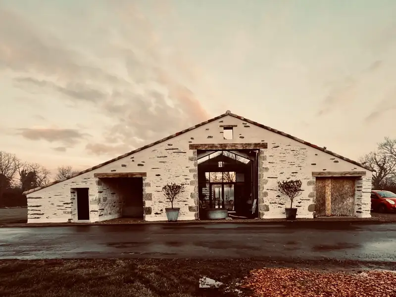 Grange en pierre rénovée au crépuscule, avec un grand portail vitré au centre