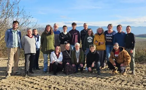 Une vingtaine de personnes posent ensemble en plein air, montagnes en arrière-plan