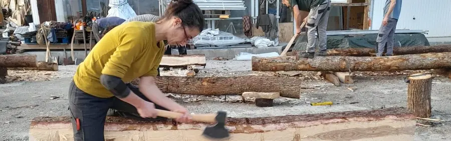 Une artisane taille un tronc à la hache sur un chantier