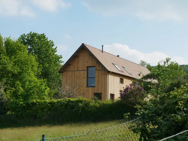 Maison à bardage bois vertical et toit de tuiles, entourée de verdure