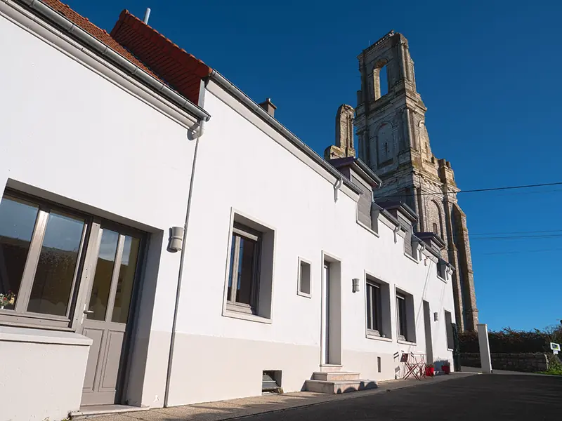Maison de bourg rénovée aux façades blanches, au pied d'un clocher en pierre