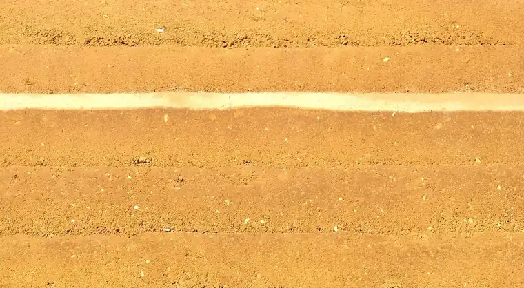 Gros plan sur un mur de terre ocre fait de couches successives, traversé d'une bande plus claire