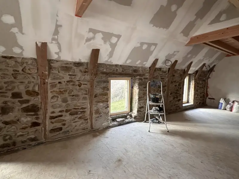 Combles en rénovation : murs en pierre apparente, poteaux en bois, plafond en cours d'enduisage