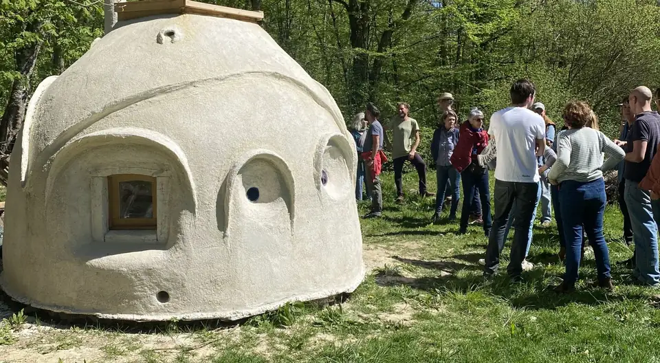 Un groupe discute à côté d'une petite construction en dôme aux murs blancs, en lisière de forêt